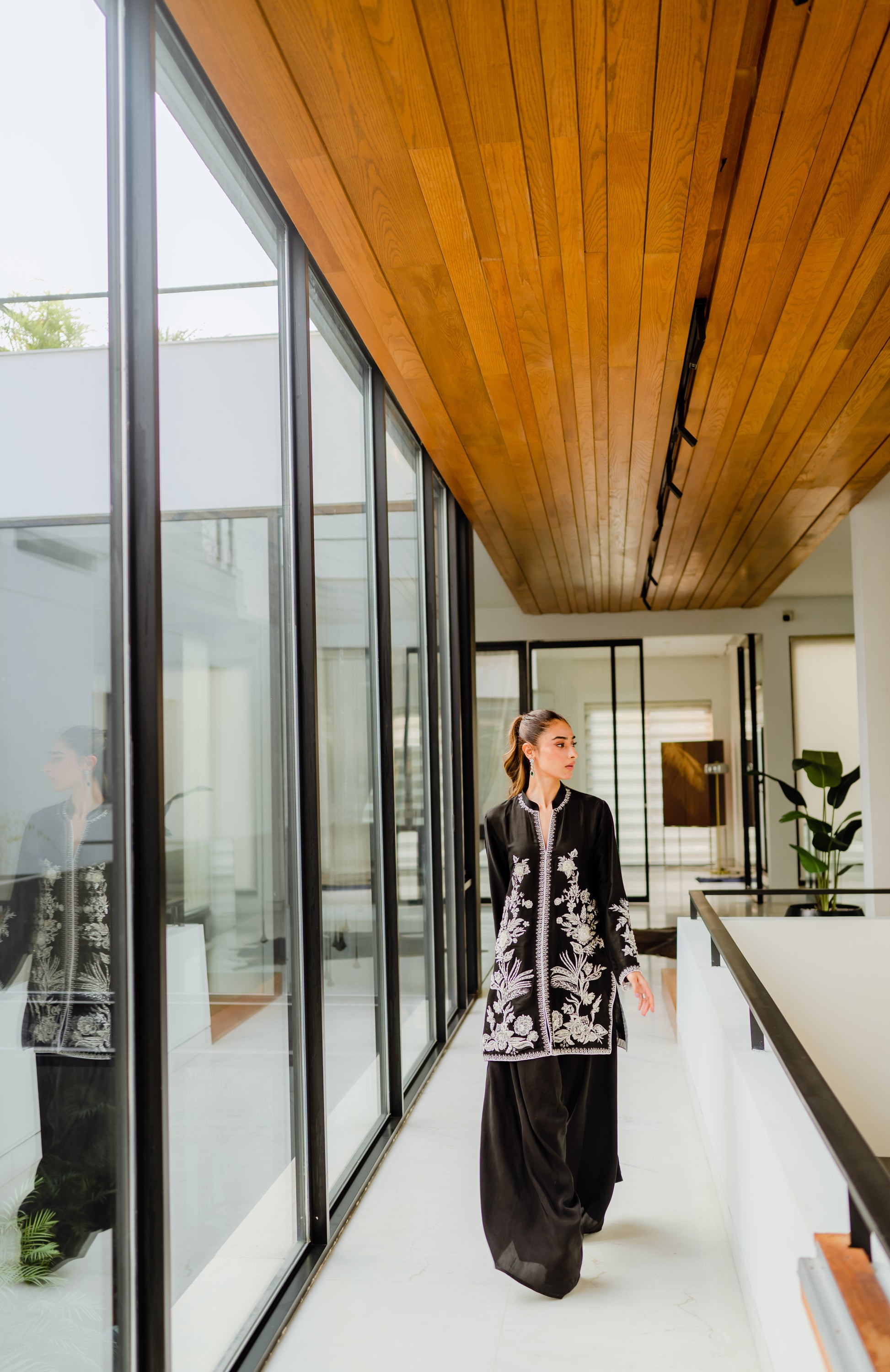 Elegant woman wearing a hand-worked black jacket with Parsi pants, ideal for party and wedding wear, in a modern setting.